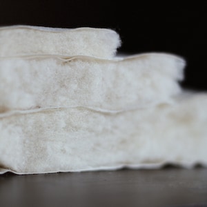 May include: Close-up of a stack of three white cotton batting layers. The batting is soft and fluffy, and the layers are slightly offset from each other.