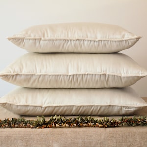 May include: Three off-white rectangular pillows stacked on top of each other. The pillows are made of a soft, smooth fabric and have a subtle sheen.