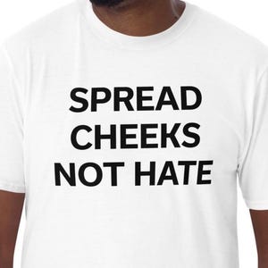 May include: White t-shirt with the message "SPREAD CHEEKS NOT HATE" printed in bold black letters. The shirt has short sleeves and a crew neck. The overall style is casual and comfortable.