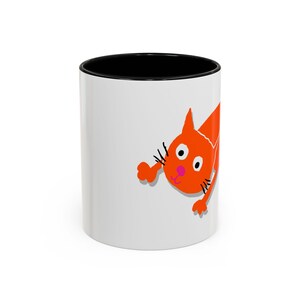 Könnte beinhalten: Weiße Keramiktasse mit schwarzem Rand und einer orangefarbenen Comic-Katze, die über den Rand schaut.