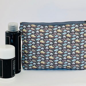 May include: A black cosmetic bag with a zipper closure, patterned with small cars in various colors. Two black bottles and a white-topped container are next to the bag, suggesting a travel or grooming set.