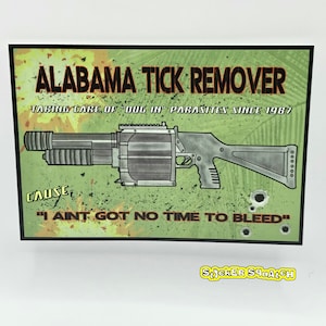 May include: A rectangular sticker with the text "ALABAMA TICK REMOVER" and a graphic of a gun. The sticker has a green and brown background with the text "TAKING CARE OF 'DOG IN' PARASITES SINCE 1987" and "I AINT GOT NO TIME TO BLEED".