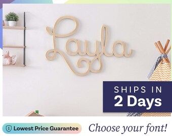 May include: A light-colored wooden wall sign featuring the name Layla in a cursive script font. The letters are connected in a single continuous piece, showcasing a smooth, natural wood grain finish mounted against a plain wall surface.