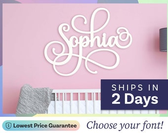 May include: A white wall-mounted sign featuring the name Sophia in a cursive script font. The lettering is displayed against a solid light pink wall above a white crib. The sign has decorative flourishes on the capital S and the lowercase a.