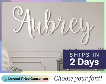 May include: A white wall-mounted sign featuring the name Aubrey in a cursive script font. The letters are connected and have a smooth finish. The sign is displayed against a neutral wall above a piece of furniture, serving as a decorative piece.
