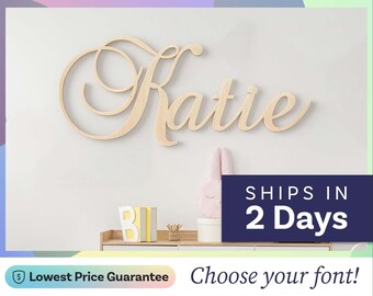 May include: A light-colored wooden wall sign featuring the name Katie in a cursive script font. The letters are connected and have a smooth, natural wood finish. The sign is mounted on a plain wall above a wooden shelf with decorative items.