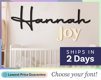 May include: A wall-mounted sign featuring the name Hannah in a black cursive script font and the word joy in a light beige serif font. The letters are mounted on a plain wall above a white crib, displaying the text 2day decor at the top.
