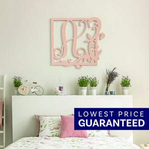May include: A light pink square wall hanging featuring a large, stylized letter A integrated with intricate, swirling vine and leaf cutouts. The decorative piece is mounted on a wall above a bed, showcasing a flat, matte finish and detailed scrollwork.