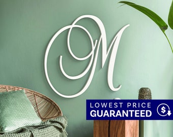May include: A large, white, cursive letter M wall decoration featuring elegant, sweeping loops and a smooth finish. The letter is mounted on a solid surface, showcasing a clean, script-style typography design that stands out with its bright white color.