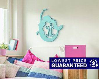May include: A light blue wall decoration shaped like a mermaid silhouette with a large letter M integrated into the center. The cutout design features smooth, curved lines and a solid matte finish, mounted on a plain wall above a bed.