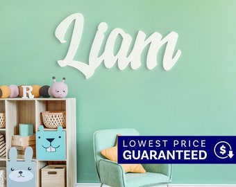 May include: A white wall-mounted sign featuring the name Liam in a cursive script font. The letters are mounted on a solid light green wall above a wooden storage unit with various toy bins and a light green upholstered armchair with a pillow.