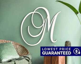 May include: A large, white, cursive letter M wall decoration featuring elegant, sweeping loops and a smooth finish. The letter is mounted on a solid surface, showcasing a clean, script-style typography design that stands out with its bright white color.