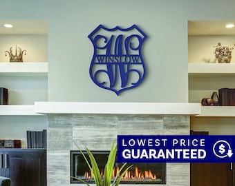 May include: A dark blue wall-mounted sign shaped like a shield featuring a large, stylized letter W with the name WINSLOW integrated horizontally across the center. The cutout design is made of a solid material and is mounted on a light wall.