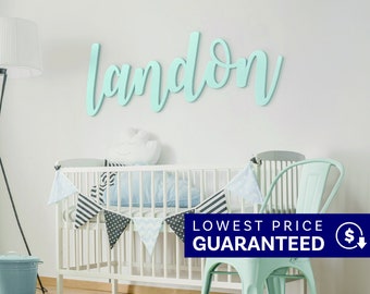 May include: A wall-mounted sign featuring the name landon in a light mint green cursive script font. The letters are connected and have a smooth finish, displayed horizontally against a plain white wall above a white crib and a mint green chair.
