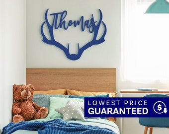 May include: A dark blue wall-mounted sign featuring the name Thomas in a cursive script integrated into the shape of a deer antler silhouette. The sign is constructed from a flat material with a visible wood grain texture throughout the surface.