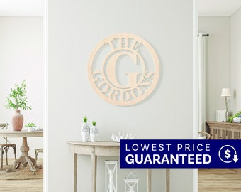 May include: A circular light-colored wooden wall sign featuring a large capital letter G in the center, with the text THE GORDONS arched along the bottom edge. The sign is constructed from a flat, laser-cut material with a smooth, natural wood finish.