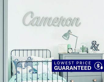 May include: A light gray wooden wall sign featuring the name Cameron in a cursive script font. The sign is mounted on a white wall above a dark metal bed frame with light blue and white bedding, a gray dresser, a desk lamp, and a clock.