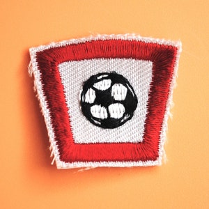 May include: A red and white embroidered patch with a black and white soccer ball in the center.