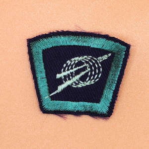 May include: A dark blue and teal embroidered patch with a white design of a rope and a needle.