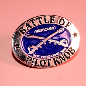 May include: A silver oval pin with the words "Battle of Pilot Knob" and "Missouri" in black lettering. The pin features a blue enamel background with crossed swords and the date "September 26-27, 1864".