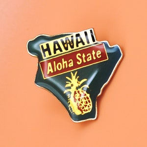 May include: A green and gold metal pin shaped like the state of Hawaii with the words "Hawaii Aloha State" and a pineapple design.