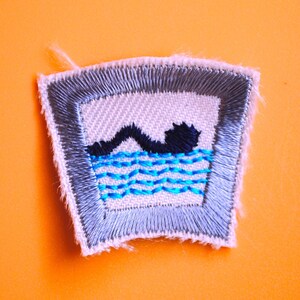 May include: A gray and white embroidered patch with a blue swimmer in a pool of water. The patch is shaped like a rounded rectangle with frayed edges.