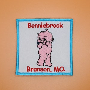 May include: A blue and white embroidered patch with the text "Bonniebrook Branson, MO." and a cartoon image of a pink baby.