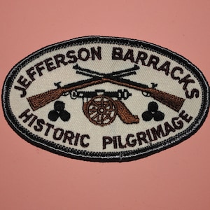 May include: A white oval patch with black and brown embroidery. The patch reads "Jefferson Barracks Historic Pilgrimage" with a cannon and two crossed rifles in the center.