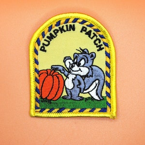May include: A yellow, blue, and orange embroidered patch with a cartoon squirrel holding a pumpkin. The patch says "Pumpkin Patch" in a blue and yellow arc.