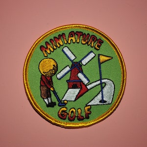 May include: A green and yellow embroidered patch with the text "MINIATURE GOLF" and a cartoon golfer putting a ball past a windmill.