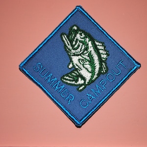 May include: A blue diamond-shaped patch with white stitching around the edges. The patch features a green and white fish with the text "SUMMER CAMPOUT" in blue.