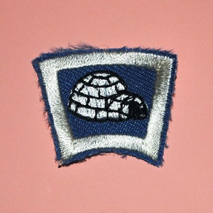 May include: A blue and white embroidered patch with a white igloo design. The patch has a white border and is slightly frayed around the edges.