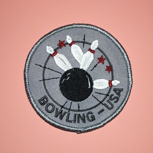 May include: A gray circular patch with a black bowling ball and white bowling pins in the center. The text "BOWLING - USA" is written around the edge of the patch.