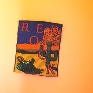 May include: A red, orange, and yellow embroidered patch with the text "RED ROCK" and a cactus and a small cactus in a desert landscape.