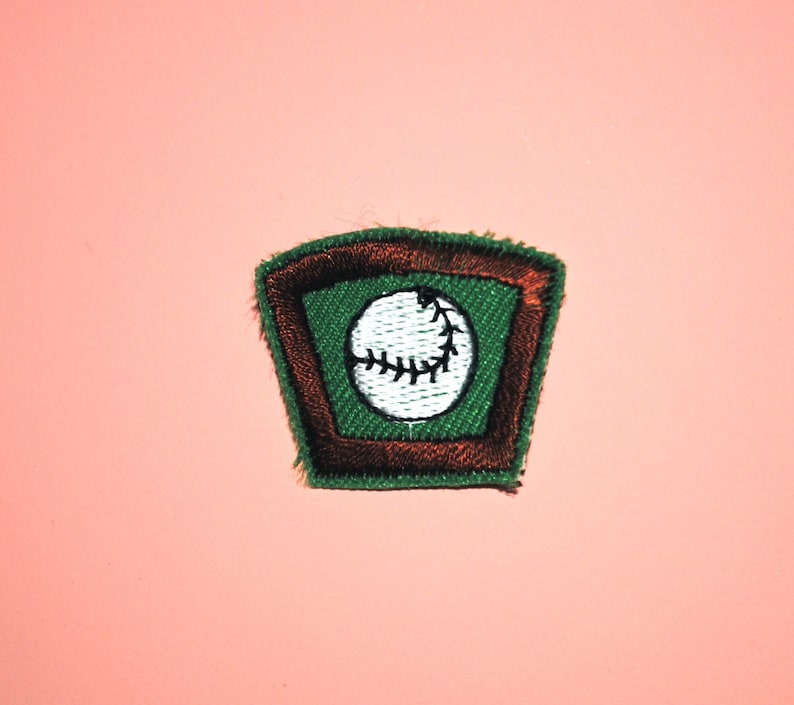 Pu&ograve; includere: Una toppa ricamata verde e marrone con una palla da baseball bianca all'interno. La palla da baseball ha cuciture nere.
