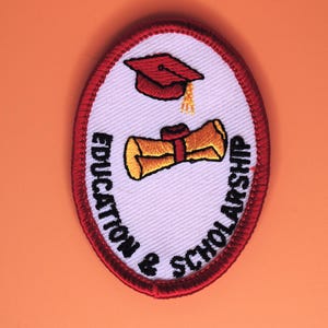 May include: Oval patch with a red border and a white center. The patch features a graduation cap and a scroll, with the words "EDUCATION & SCHOLARSHIP" in black lettering around the edge. The background is a solid orange color.