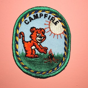 May include: A green, yellow, and blue embroidered patch with a cartoon tiger, a campfire, and the text "Campfire".