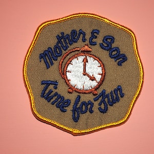 May include: A brown and yellow embroidered patch with a clock and the text "Mother & Son Time for Fun".