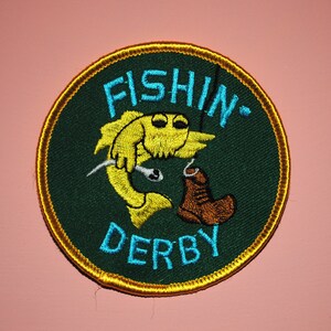 May include: A green and gold embroidered patch with a yellow fish and the text "FISHIN' DERBY".