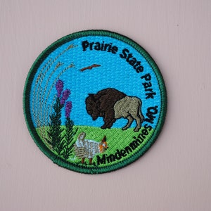 May include: A green and blue embroidered patch with the text "Prairie State Park, O.W.S. Mindenmines" and a depiction of a bison, a bird, and some grass.