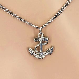 May include: A silver-toned metal necklace featuring a pendant shaped like a nautical anchor. The anchor design includes a detailed rope wrapped around the central shaft and flukes. The pendant hangs from a matching silver-toned metal chain link.