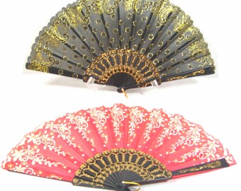 May include: Two decorative folding fans. One fan is black with gold glitter and a paisley design. The other fan is pink with white floral designs. Both fans have black and gold trim.