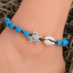 May include: A turquoise and brown beaded ankle bracelet with a silver turtle charm and a white seashell charm.