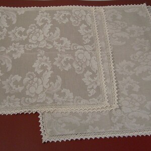 May include: Two white crocheted tablecloths with a floral pattern. The tablecloths are square and have a scalloped edge.