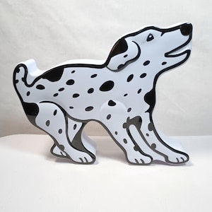 May include: A white ceramic Dalmatian figurine with black spots and accents. The dog is posed in a playful stance, with its head raised and mouth open. The figurine has a glossy finish and is a decorative item.
