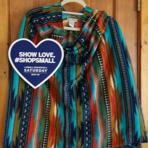 May include: A blue, red, orange, and turquoise patterned fleece blanket with a heart-shaped tag that says "Show Love, #ShopSmall - Small Business - Saturday, Nov 24".