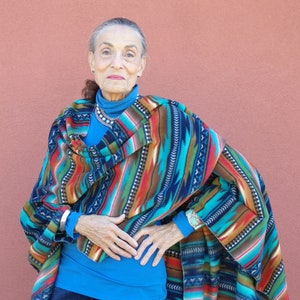 May include: A woman wearing a colorful striped poncho with a blue shirt and jeans.