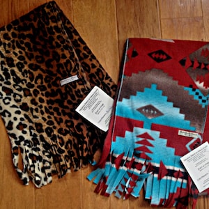 May include: Two fleece scarves with fringe. One scarf has a leopard print pattern. The other scarf has a turquoise, red, and brown geometric pattern. Both scarves have tags attached.