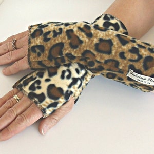 以下が含まれることがあります： 茶色、黒、白のヒョウ柄フリース製リストウォーマーのペア。リストウォーマーには、「Fabulous Fleece」と「Santa Fe, NM」と書かれた白いタグが付いています。