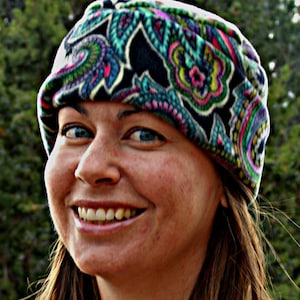 May include: A woman wearing a colorful paisley patterned fleece headband. The headband is black, green, pink, and blue.
